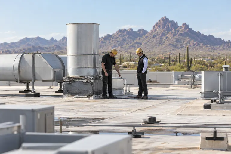 Roofer and manager standing beside a large exhaust stack on a commercial roof